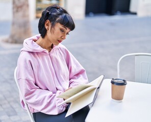 Young woman reading book sitting on table at coffee shop terrace