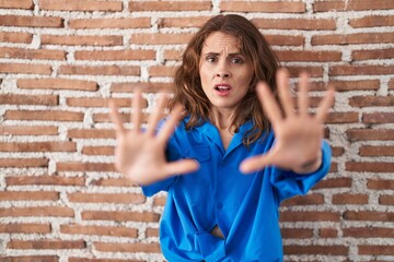 Beautiful brunette woman standing over bricks wall doing stop gesture with hands palms, angry and frustration expression