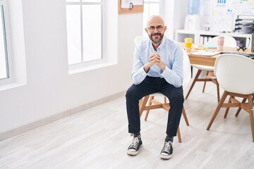 Young bald man business worker smiling confident sitting on chair at office