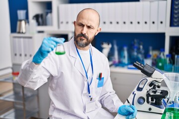 Young bald man scientist holding test tube writing on notebook at laboratory