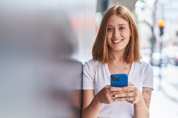 Young redhead woman smiling confident using smartphone at street