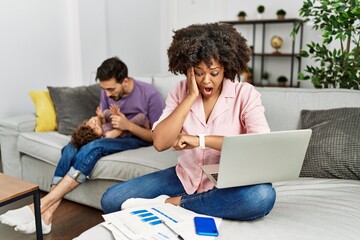 Mother of interracial family working using computer laptop at home looking at the watch time...