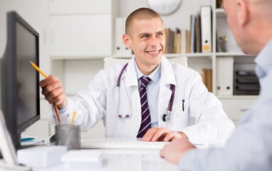 Male doctor who practices in the clinic consults the patient, explaning in detail the nuances of...