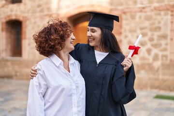 Two women mother and daughter hugging each other holding diploma at campus university
