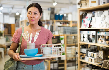 Asian woman walking through hall of housewares store and holding tray with tableware on it in hands.