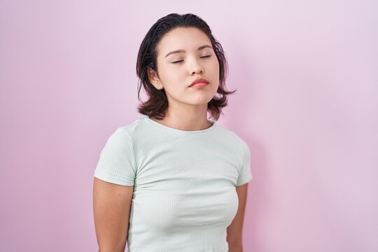 Hispanic young woman standing over pink background looking sleepy and tired, exhausted for fatigue and hangover, lazy eyes in the morning.