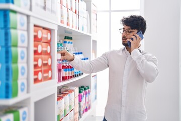 Naklejka na ściany i meble Young hispanic man client talking on smartphone at pharmacy