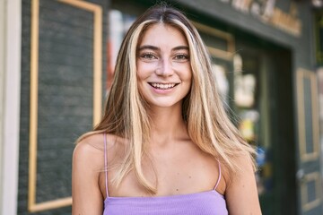 Young blonde girl smiling happy standing at the city.
