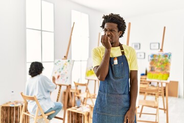 African young man standing at art studio looking stressed and nervous with hands on mouth biting nails. anxiety problem.