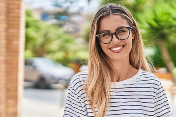 Young blonde woman smiling confident wearing glasses at street