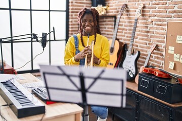 African american woman musician smiling confident holding trumpet at music studio