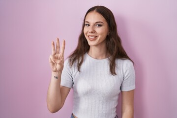 Young hispanic girl standing over pink background showing and pointing up with fingers number three while smiling confident and happy.