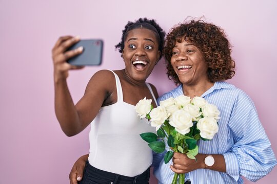 Two african women taking a selfie photo with flowers celebrating crazy and amazed for success with open eyes screaming excited.