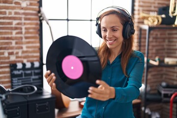 Young woman artist listening to music holding vinyl disc at music studio