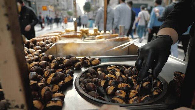 Delicious chestnut grilling over glowing coals, make street food in Istanbul. Barbecued roasted on the hot stove fresh tasty chestnut, male hand flips 
