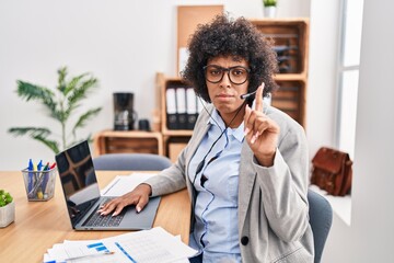 Black woman with curly hair wearing call center agent headset at the office pointing up looking sad and upset, indicating direction with fingers, unhappy and depressed.