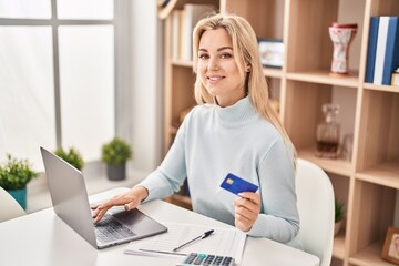 Fototapeta premium Young blonde woman using laptop and credit card sitting on table at home