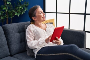 Middle age woman using touchpad sitting on sofa at home