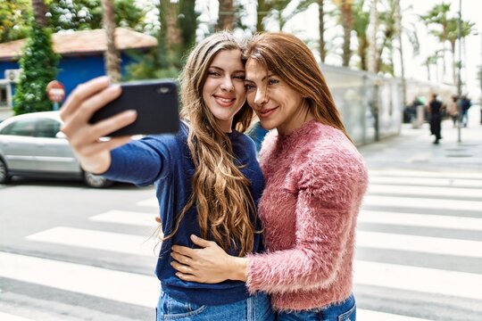 Mother and daughter hugging each other and making selfie by the smartphone at street