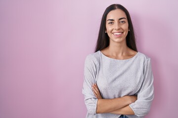 Fototapeta premium Young brunette woman standing over pink background happy face smiling with crossed arms looking at the camera. positive person.