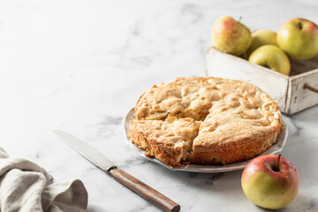 Traditional Charlotte with apples and rustic knife on white marble background, apple pie. Text space