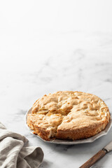 Traditional Charlotte with linen napkin and rustic knife on white marble background, apple pie. Text space
