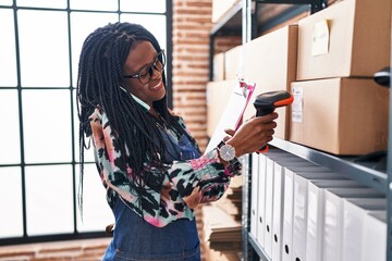 African american woman ecommerce business worker scanning package talking on smartphone at office