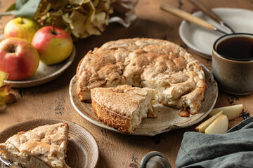 Traditional apple pie charlotte sprinkled with cinnamon on wooden background. Tea time with apple dessert, autumn moody still life