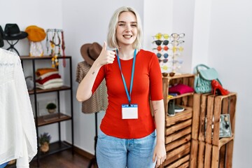Young caucasian woman working as manager at retail boutique doing happy thumbs up gesture with hand. approving expression looking at the camera showing success.