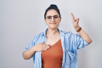 Young modern girl with blue hair standing over white background smiling swearing with hand on chest and fingers up, making a loyalty promise oath