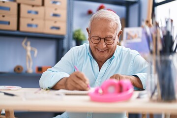 Fototapeta na wymiar Senior grey-haired man artist smiling confident drawing on notebook at art studio