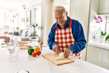 Senior man smiling confident cutting onion at kitchen