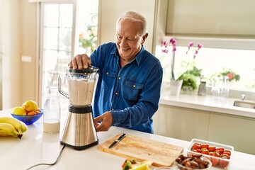 Senior man smiling confident shaking blender at kitchen