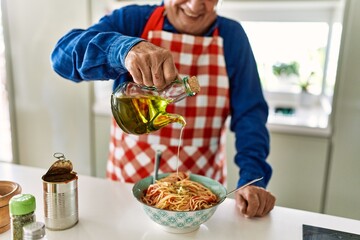 Senior man smiling confident pouring oil on spaghetti at kitchen