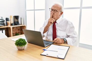 Senior man working at the office using computer laptop asking to be quiet with finger on lips....
