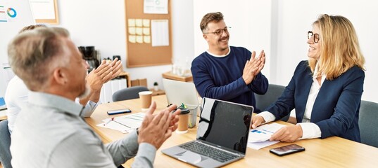 Group of middle age business workers smiling and clapping to partner at the office.