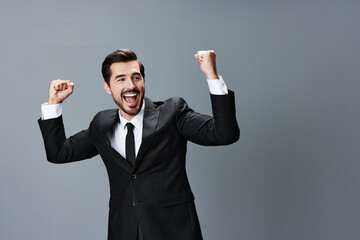 Business man happy smile with teeth open mouth raised hands up fists bump winner on gray background in business suit.