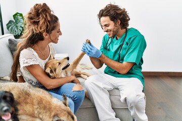 Man and woman wearing veterinarian uniform examining hoof dog at home