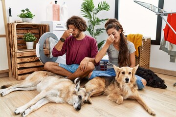 Young hispanic couple doing laundry with dogs tired rubbing nose and eyes feeling fatigue and...