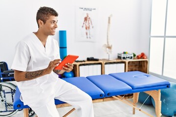 Obraz premium Young hispanic man working as physiotherapist using touchpad at physiotherapy room