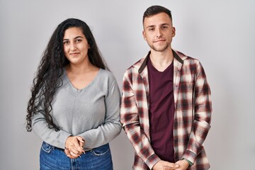 Young hispanic couple standing over white background with hands together and crossed fingers smiling relaxed and cheerful. success and optimistic