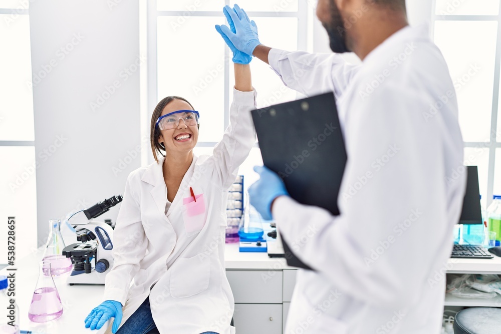 Wall mural Man and woman scientist partners holding clipboard high five raised up hands at laboratory