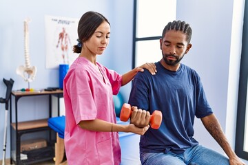 Fototapeta premium Man and woman wearing physiotherapist uniform having rehab session using dumbbell at physiotherpy clinic