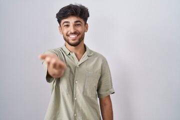 Arab man with beard standing over white background smiling cheerful offering palm hand giving assistance and acceptance.