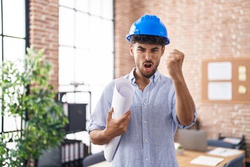 Arab man with beard wearing architect hardhat at construction office annoyed and frustrated shouting with anger, yelling crazy with anger and hand raised