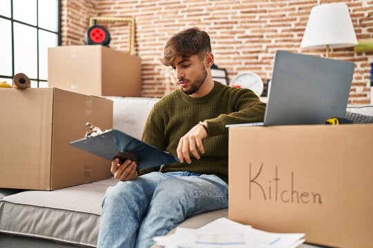 Young arab man using laptop reading document at new home