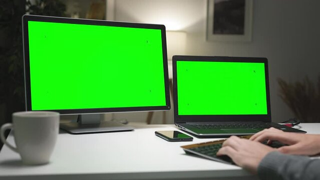 Young gamer sitting at home and playing using two chromakey screens. Freelancer working on project, programmer writing code