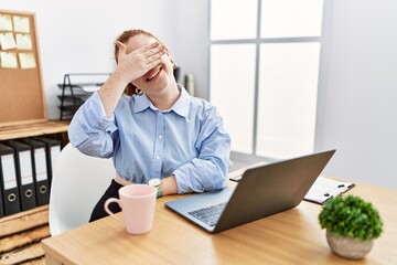 Young redhead woman working at the office using computer laptop smiling and laughing with hand on face covering eyes for surprise. blind concept.