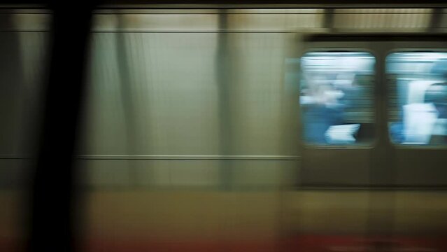 Subway train with people inside moving fast from metro station, close up. Windows of train passing at underground station