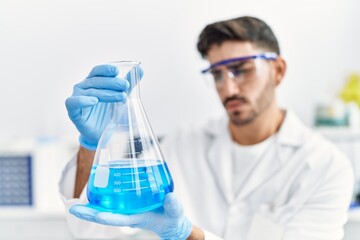 Handsome hispanic man working as scientific holding erlenmeyer flask at laboratory